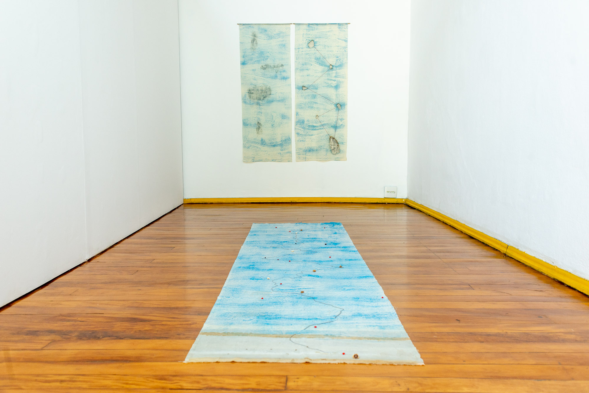 Blue textile installation with tree bark imprints and clay traces in exhibition space. Produced during a residency at Instituto Inclusartiz, Rio de Janeiro, Brazil